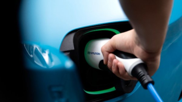 Person inserting a charging plug into a blue electric car.