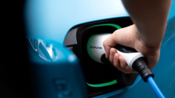Hand plugging in a charging cable to a blue electric vehicle.