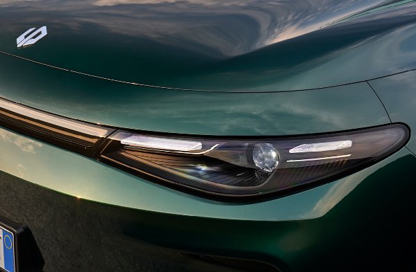 Close-up of a green car’s front showing a headlight and badge.