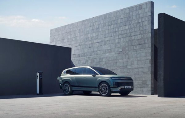 Electric SUV parked near a charging station between modern architectural walls.