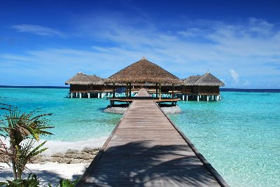 Wooden walkway leading to overwater bungalows on a clear blue sea.