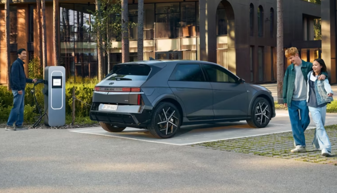 Electric car charging, with a person plugging in and a couple walking nearby.