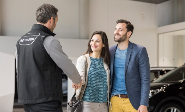 Man and woman shaking hands with a Hyundai dealer in a car showroom.