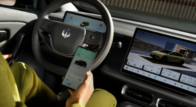 Person in driver's seat using a smartphone, with car dashboard and two screens visible.
