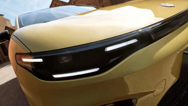 Close-up of the front left headlight and grille of a yellow car.