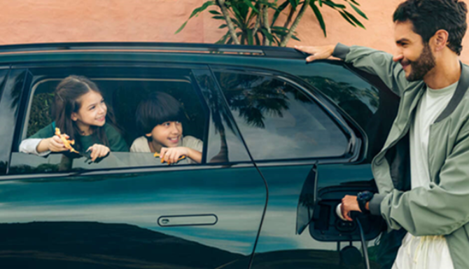 Man charges electric car while two children look out of the rear window.