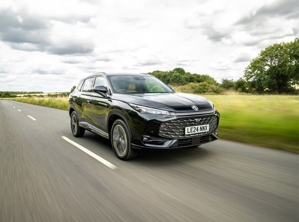 A black SUV driving on a rural road with trees and grass on either side.
