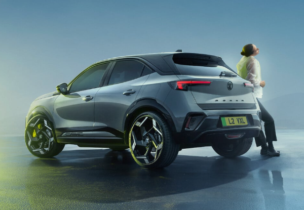 Silver SUV with black roof, viewed from the rear three-quarters, with a person leaning against it.