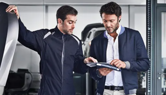 Two men discussing over a notepad in a car workshop.