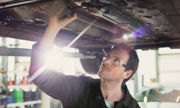 Mechanic wearing safety glasses inspecting underneath a car on a lift.