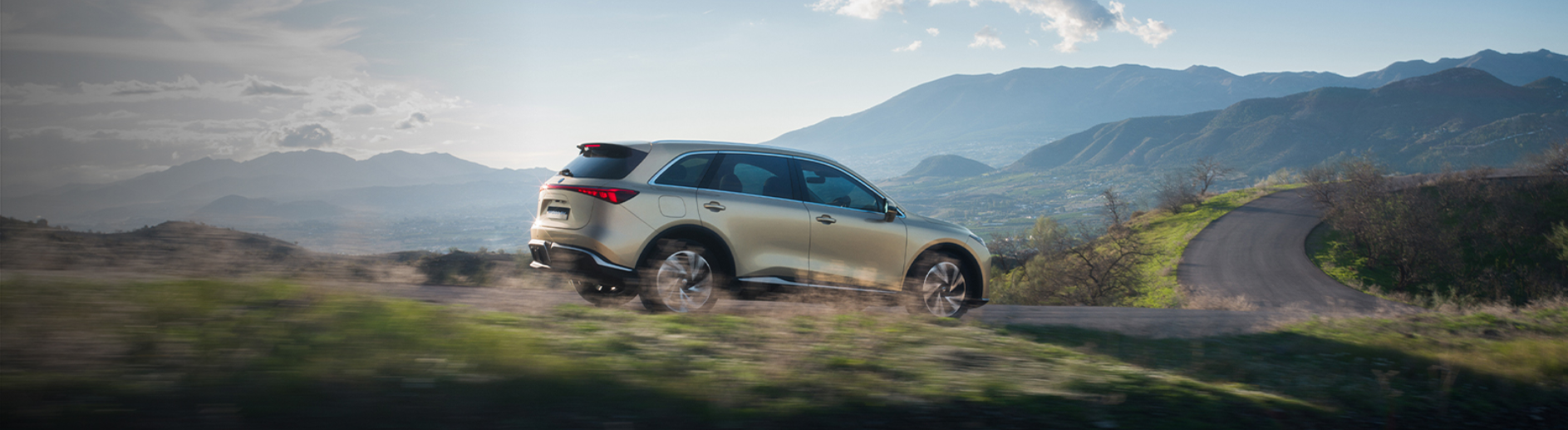 A gold SUV driving on a rural road with mountains in the background.