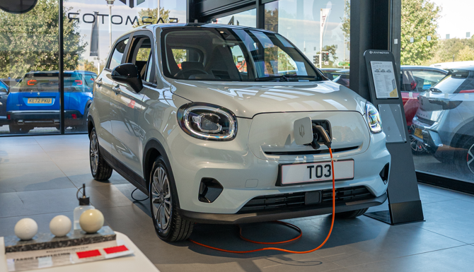 Electric car on display in a showroom, plugged in and charging.